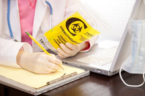 Doctor checking medication. Cancer, leukemia patient medicine. Laptop. Doctor checking medication used by leukemia cancer patient.  She holds empty medicine bag while verifying dosage against patient records on laptop computer. Gloves, stethoscope.  technology office equipment laboratory stock pictures, royalty-free photos & images