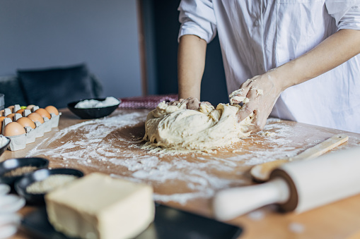 A woman kneads dough on a wooden kitchen table. Unrecognizable person.