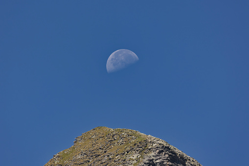 View of the top of a mountain and the Moon in the background.