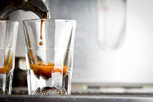 Dual espressos being made from a commercial machine, shallow depth of field. The brew is in the crema stage with fast shutter speed freezing the individual droplets of coffee cascading into the shot glass.
