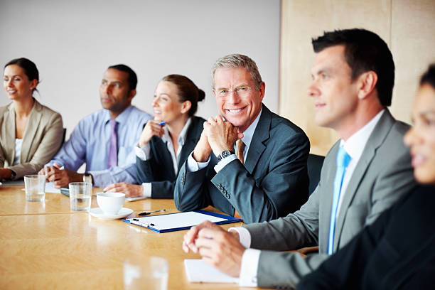 lächelnd leitender geschäftsmann mit seinem team in einem meeting - board room senior adult clothing smiling stock-fotos und bilder