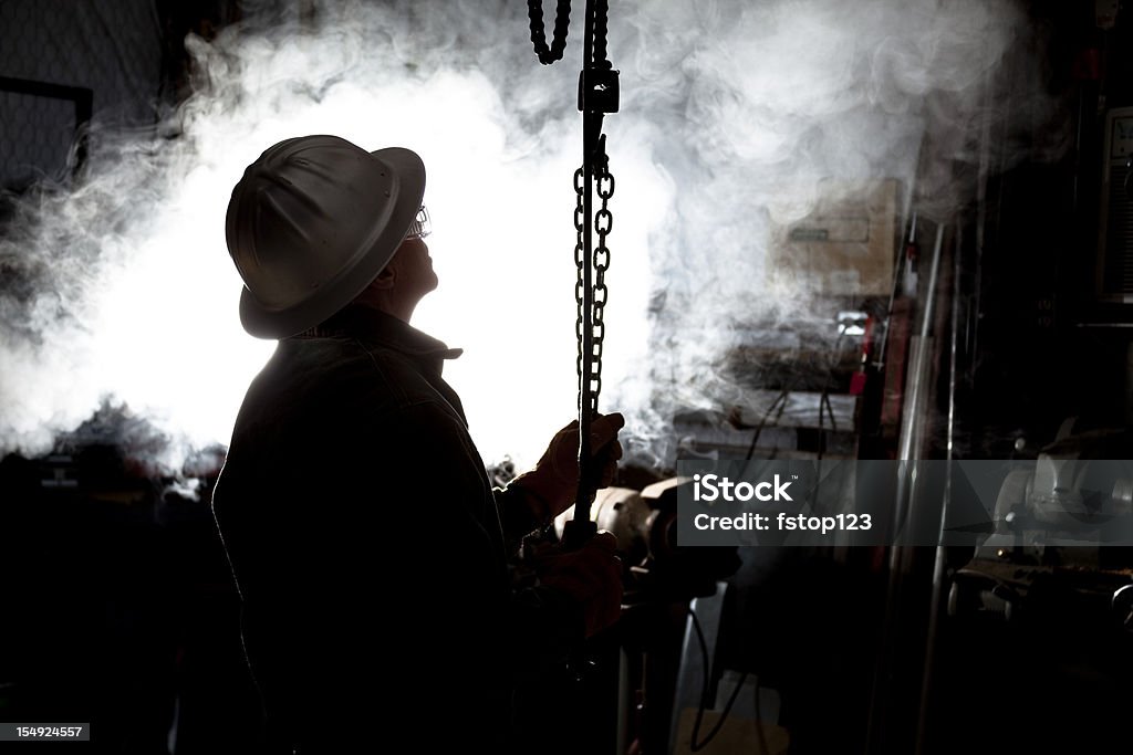 Silhouette di uomo con catena sollevatore in officina. - Foto stock royalty-free di Operaio addetto all'estrazione di petrolio