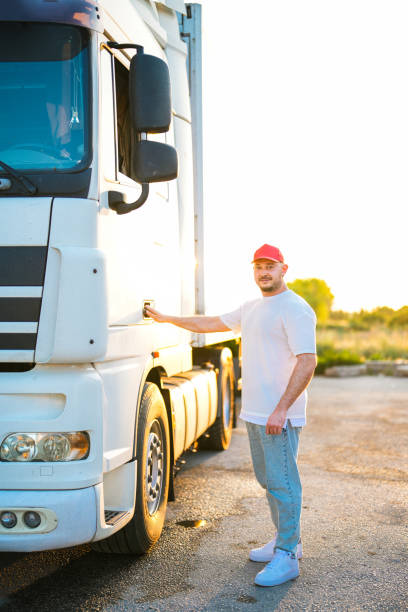 motorista de chapéu vermelho parado ao lado de caminhão branco ao pôr do sol - semi truck driver pride white - fotografias e filmes do acervo