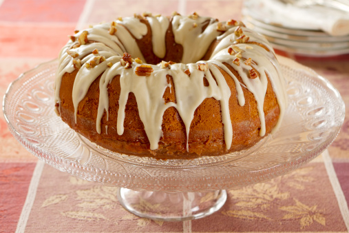 A spice bundt cake with pecans and golden raisins, frosted with a cream cheese and maple syrup glaze.