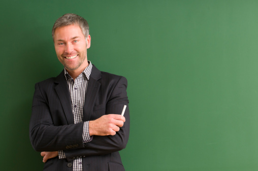 smiling teacher holding a chalk at blackboard