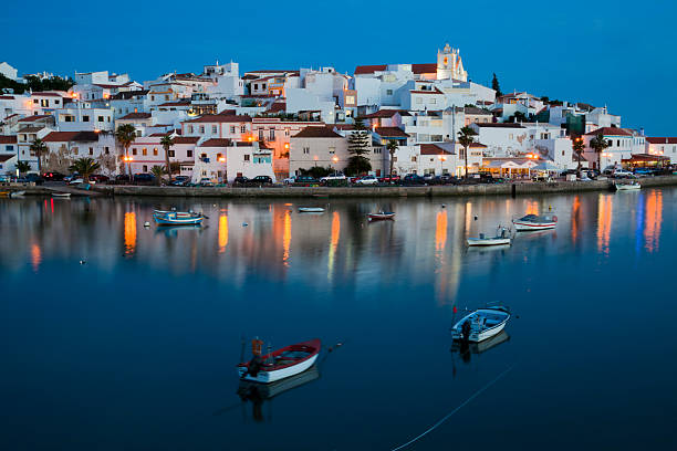 Water view of illuminated cityscape of Ferragudo in Algarve Fishing boat with Ferragudo village in the background. algarve stock pictures, royalty-free photos & images
