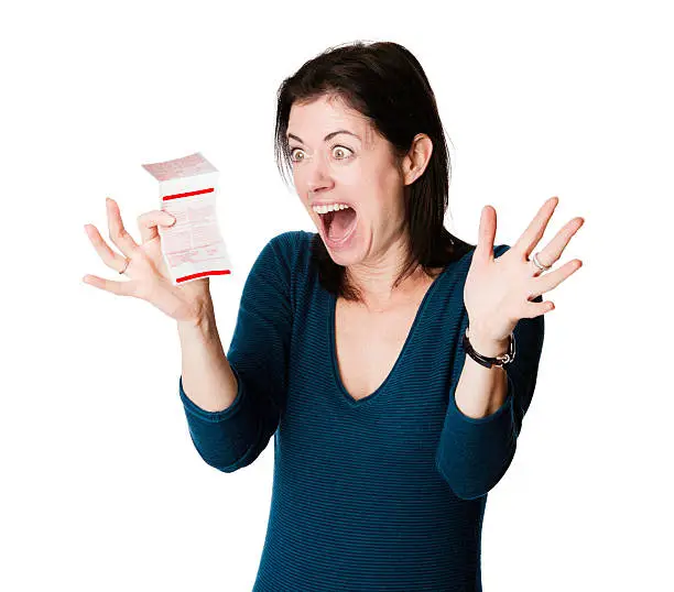 Elated woman reacts with intense enthusiasm to her winning lottery ticket. Photographed in front of a white background.