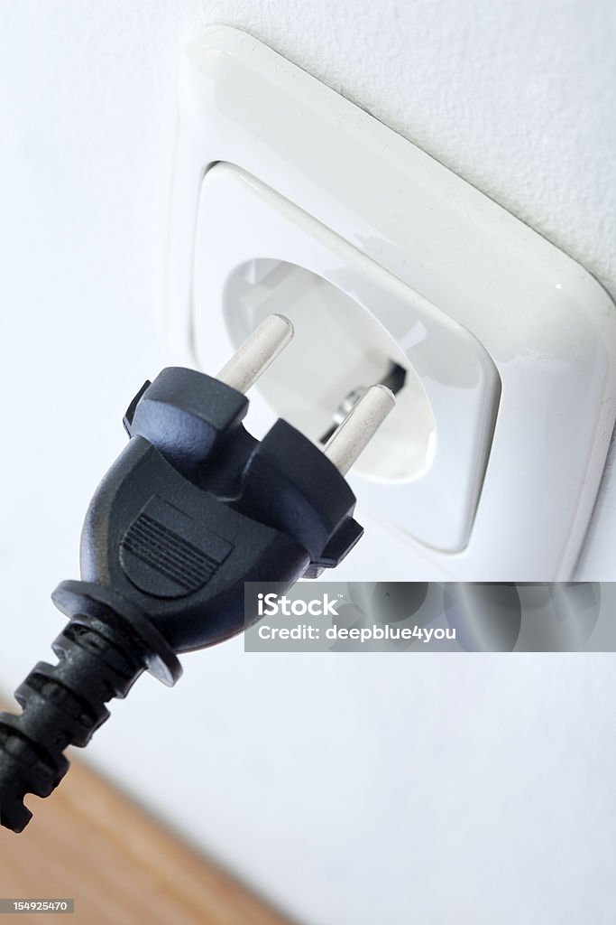 Black plug and white socket outlet on a white wall with black plug in front, raw, low sharpening, shallow depth o field with fokus on the copper pins Plugging In Stock Photo