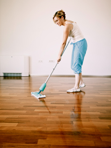 Young woman cleaning wooden floor.