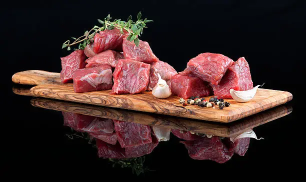 Photo of Red meat on wooden board, against black background