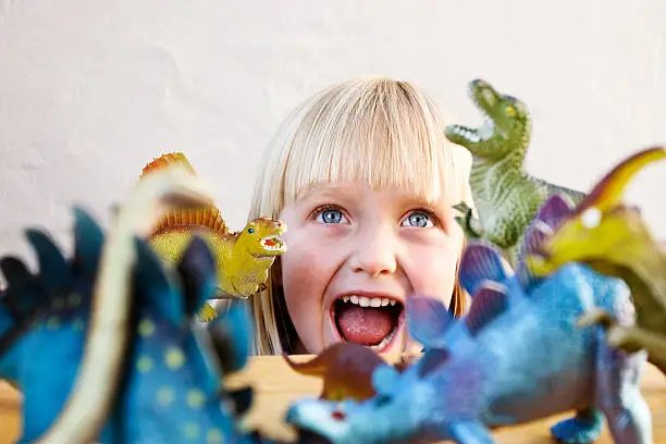 Photo of Cute blonde toddler roars at her ferocious toy dinosaurs