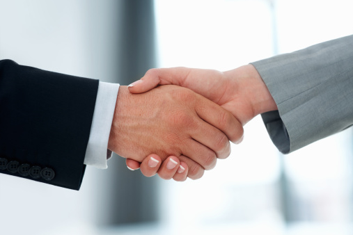 Handshake on light grey background, copy space. Businessmen wear smart suits. Business and agreement concept. Male hands shaking tight in a deal, close up.