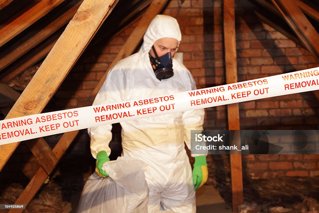 man removing asbestos A worker wearing protective clothing while clearing the hazardous substance,asbestos,from an old attic. Asbestos Stock Photo