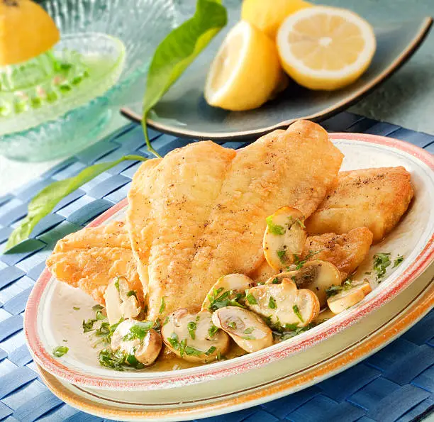 Two breaded and fried sole fillets served with baked mushrooms.Lemons in the background.