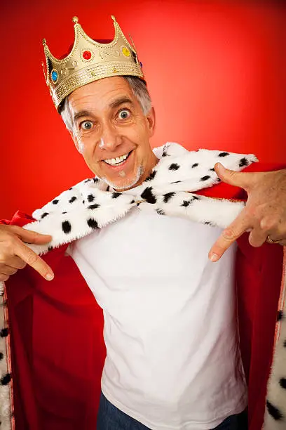 senior man wearing a king's robe and crown, pointing at his white t-shirt