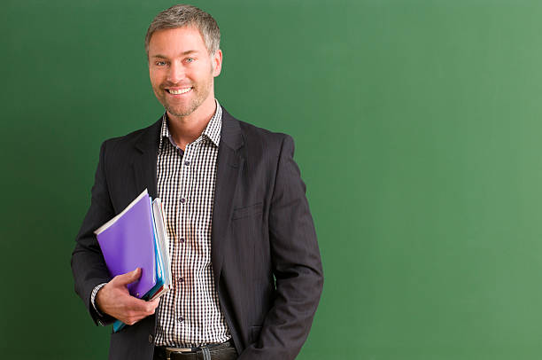 istock Teacher carrying books and standing by the blackboard 154925974