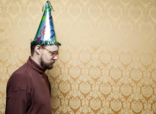 A man in a brown turtleneck stands in front of a vintage damask wallpaper background on his birthday, looking sad and dejected.  Brown and yellow color themes.  Horizontal with copy space.