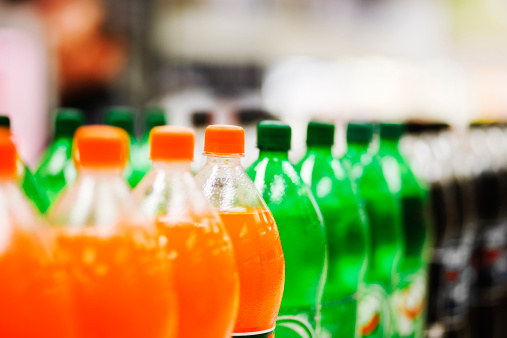 A long line of unbranded soda bottles in various flavours and colors, the focus on the center of the line.