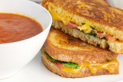 Grilled bacon, cheese and spinach sandwich with white bowl of tomato soup