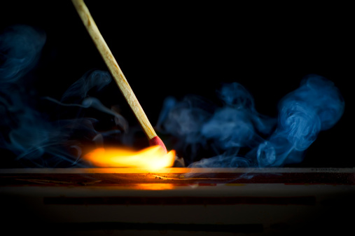 Macro shot of a wooden safety matchstick burning with a bright colorful flame on black background