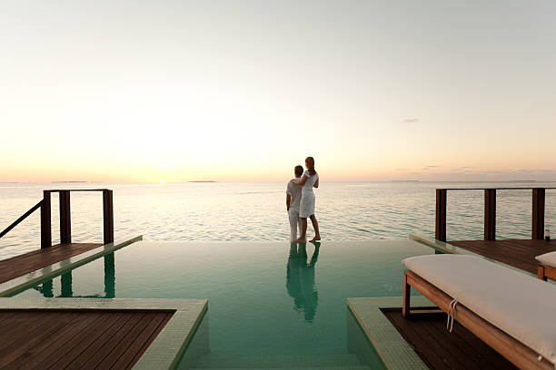 Couple enjoying the sunset at poolside couple enjoying sunset over sea on poolside of overwater bungalow bungalow photos stock pictures, royalty-free photos & images