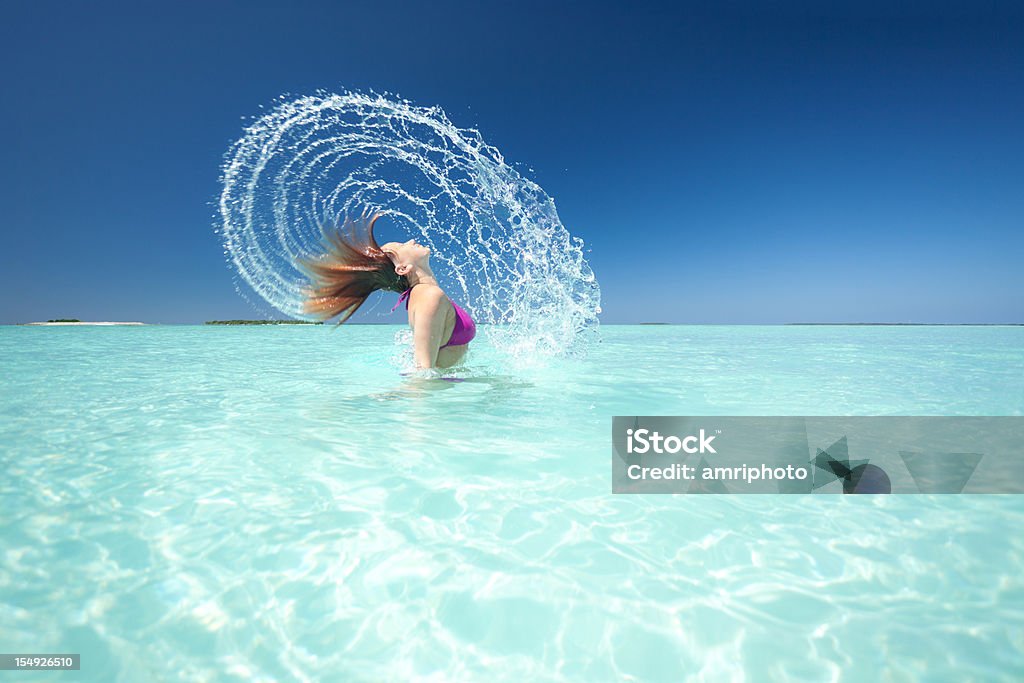 woman splashing water in lagoon woman in bikini splashing fountain of water with her hair in tropical lagoon Beach Stock Photo