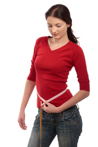 Teenage girl measuring her slim waist with measuring tape, looking down. Isolated on white.