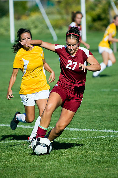 Female Soccer Player in Dark Red Breaks Away From Defender stock photo