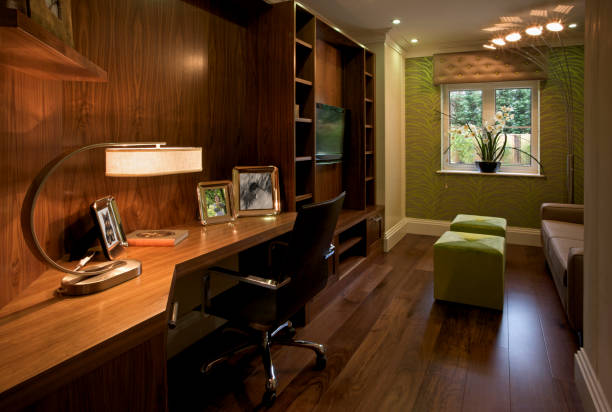home office A beautiful dark-wood paneled office room in a luxury penthouse apartment. The flooring is made from solid walnut. This is a show home for a luxury development and has been furnished by an interior designer. Two green footstool cubes are illuminated by an unusual corner lamp unit. A large desk lamp illuminates the desk top. All framed images are included in my iStock portfolio. gold desk lamp stock pictures, royalty-free photos & images