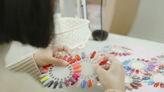 Young Asian woman customer choosing nail polish color swatch, manicure in nail beauty salon