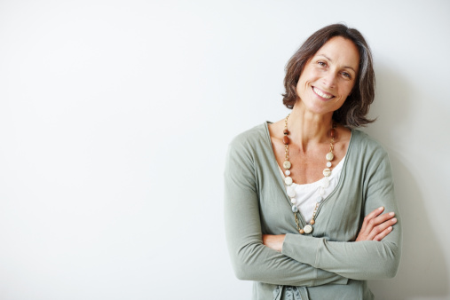 Head and shoulders view of smiling middle aged woman in blue sweater against beige wall
