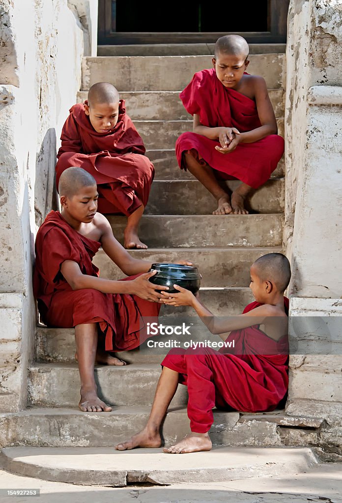 Young monks sitting on a stairway Four young monks from Bagan, Myanmar, sitting on a stairway with a bowl of alms. Yangon Stock Photo