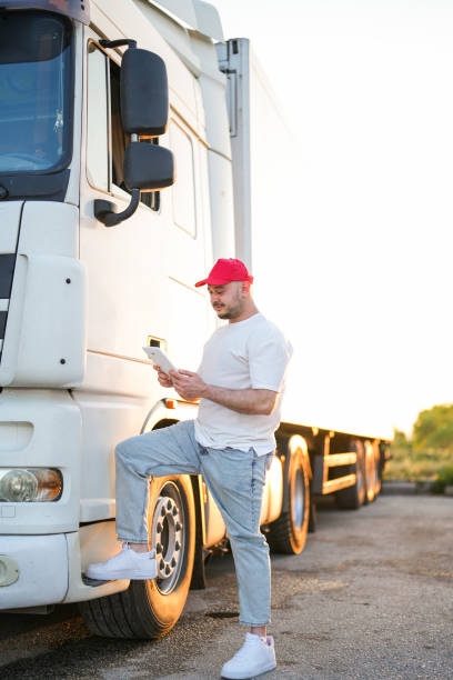 homem do motorista com tablet na mão na tampa vermelha em pé perto do caminhão branco - semi truck driver pride white - fotografias e filmes do acervo