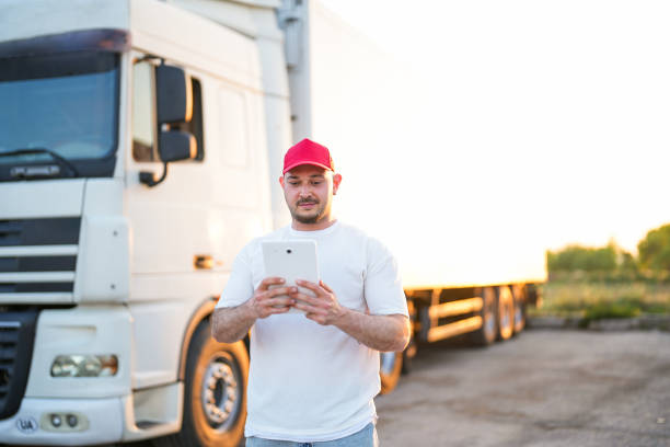 homem de chapéu vermelho em pé na frente do caminhão branco no pôr do sol segurando tablet - semi truck driver pride white - fotografias e filmes do acervo