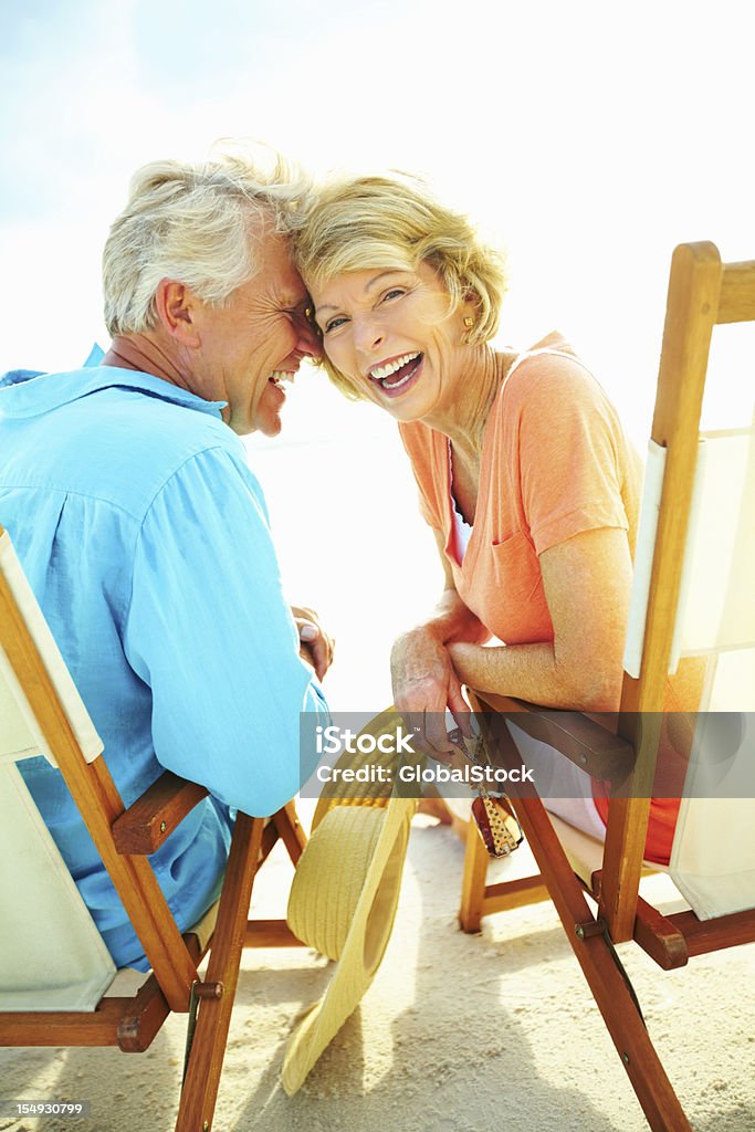 Couple laughing while enjoying the beach Retired couple in beach chairs with woman looking at camera Fun Stock Photo