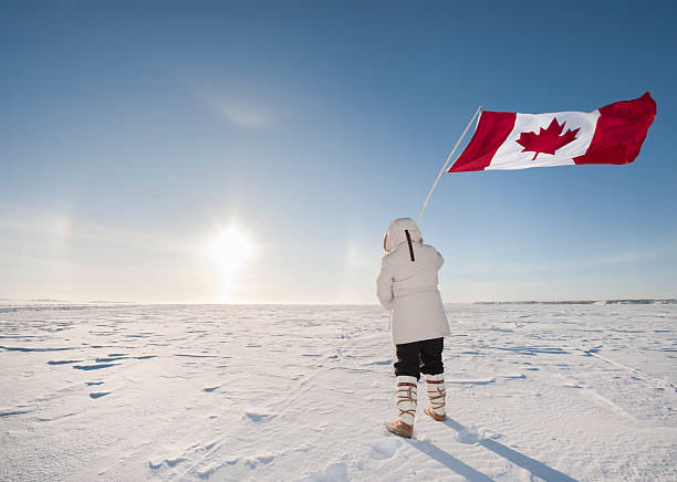 Arctic Sundog or Parhelion, Woman and Canadian Flag. At -40C, a woman waves the Canadian flag while watching a rare display in the sky known as "Sundogs".  The bright center is the actual sun with the mirror images of it reflected in suspended ice crystals in the atmosphere.   This was taken on Great Slave Lake near Yellowknife in Canada's Arctic. great slave lake stock pictures, royalty-free photos & images