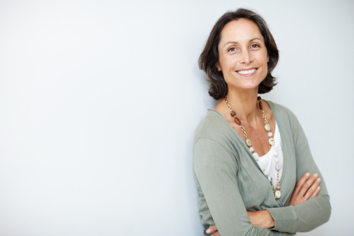 Smiling senior businesswoman with hands in pockets posing confidently on isolated white background