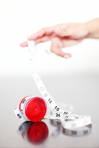 Concept shot of a woman holding a yo yo.Instead of a string it is a tape measure , to illustrate how trying to control our weight involves lots of ups and downs