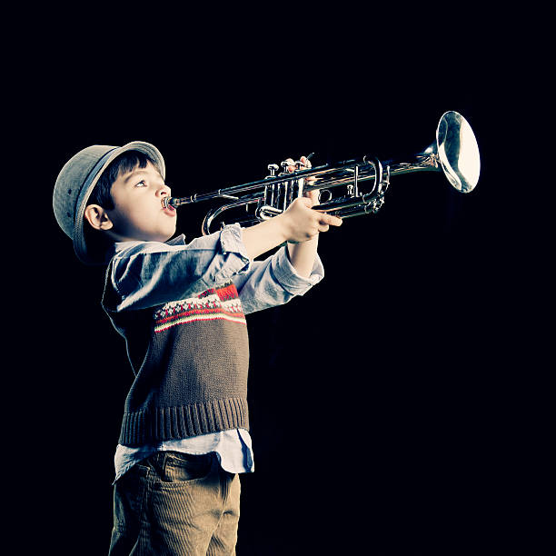 small boy dress with cool clothes and wearing hat, he is pretending to be playing the trumpet.