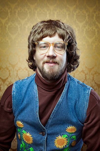 Goofy Hippy Professor A portrait of a man straight out of the 1960's and 70's, complete with shaggy hair, turtleneck, and sunflower jean vest.  Damask floral wallpaper in the background. turtleneck photos stock pictures, royalty-free photos & images