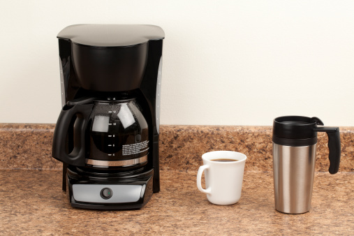 Coffee maker, coffee cup, and stainless steel travel mug, on kitchen counter. One for here and one to go.  