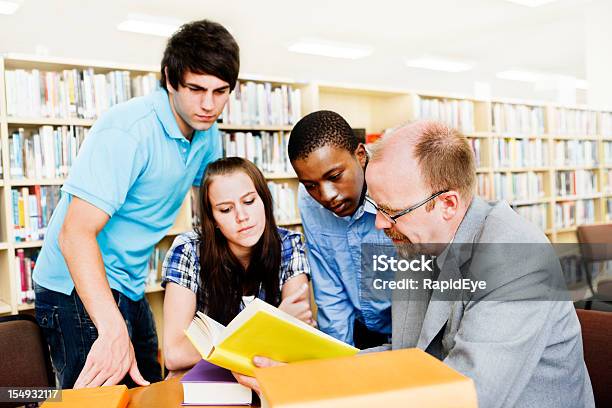 Tre Studenti E Insegnante Di Lavorare Insieme Nella Libreria - Fotografie stock e altre immagini di Adulto