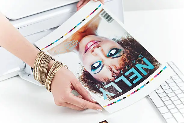 Female hand taking printout of the cover of Beauty/Fashion Magazine from printer. 