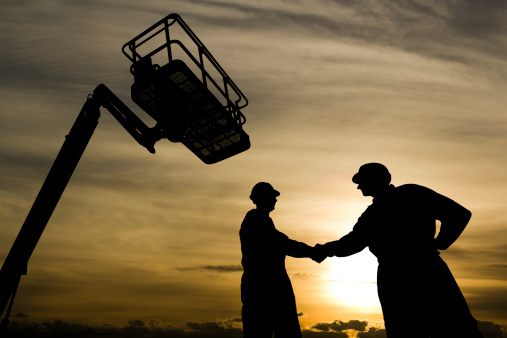 A royalty free image from the construction industry of two construction workers shaking hands underneath a cherry picker.
