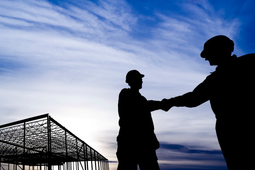 A royalty free image from the construction industry of two workers shaking hands at a construction site.