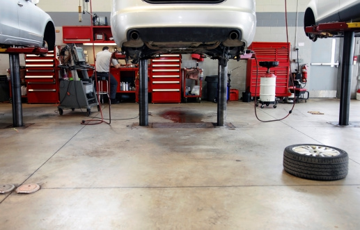 The interior of a car dealership repair facility, shows two cars on hoists.