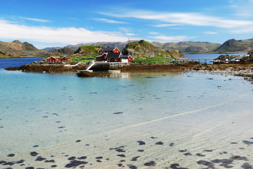 Fishing village is in the small island surrounded with blue fjord. Mageroya is photographed during low tide in summer. There are several wooden houses, motorboats, mossy hills and a lot of transparent water.