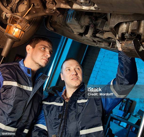 Foto de Dois Mecânicos Trabalhando Sob Automóvel Em Workshop e mais fotos de stock de Adulto