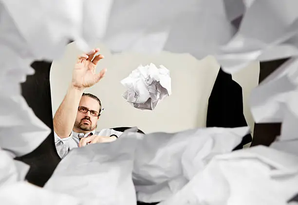 An office working throwing a crumpled piece of paper into a wastepaper basket. Viewed from within the basket.