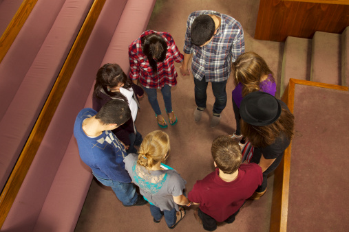8 teens seen directly above both boys and girls worship in church holding hands and praying with heads bowed